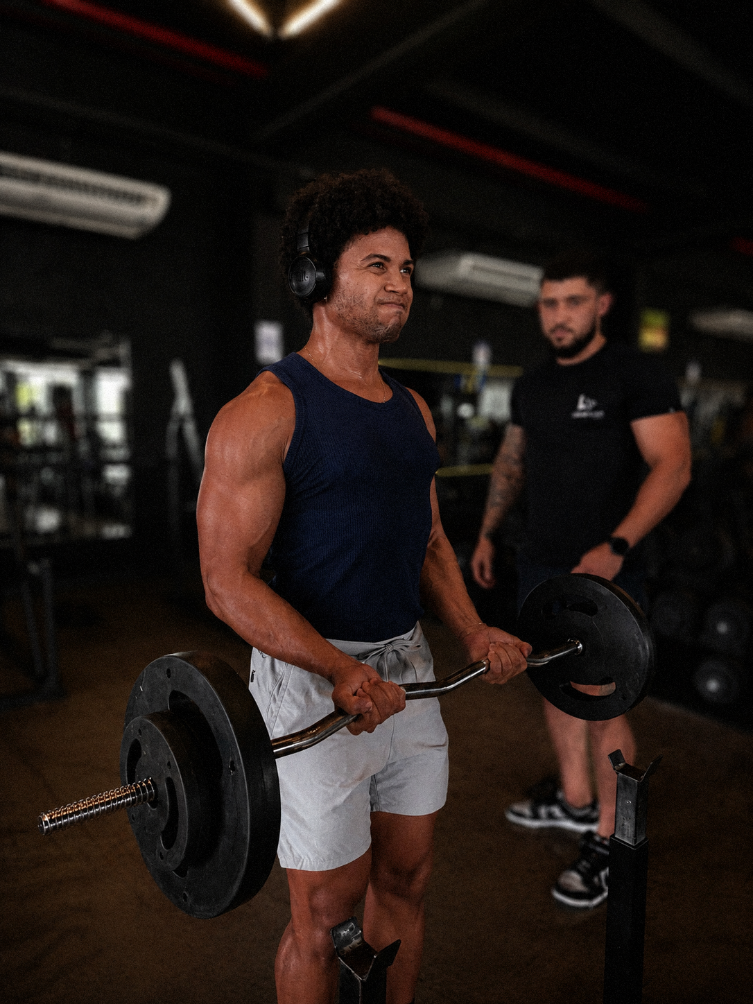 Aluno realizando exercício com barra sob acompanhamento na academia